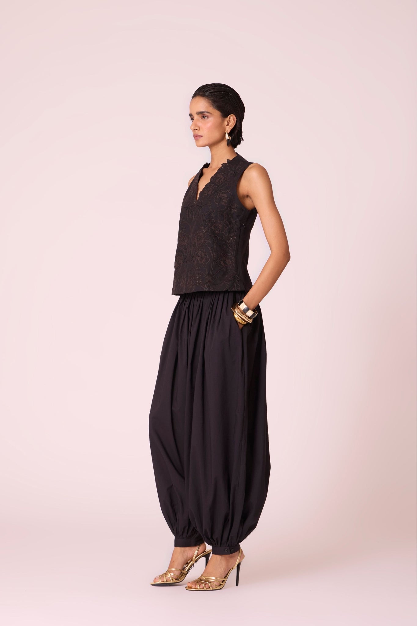 Black organic cotton pleated pants with a relaxed fit, side zip fastening, and adjustable hem cuffs.
