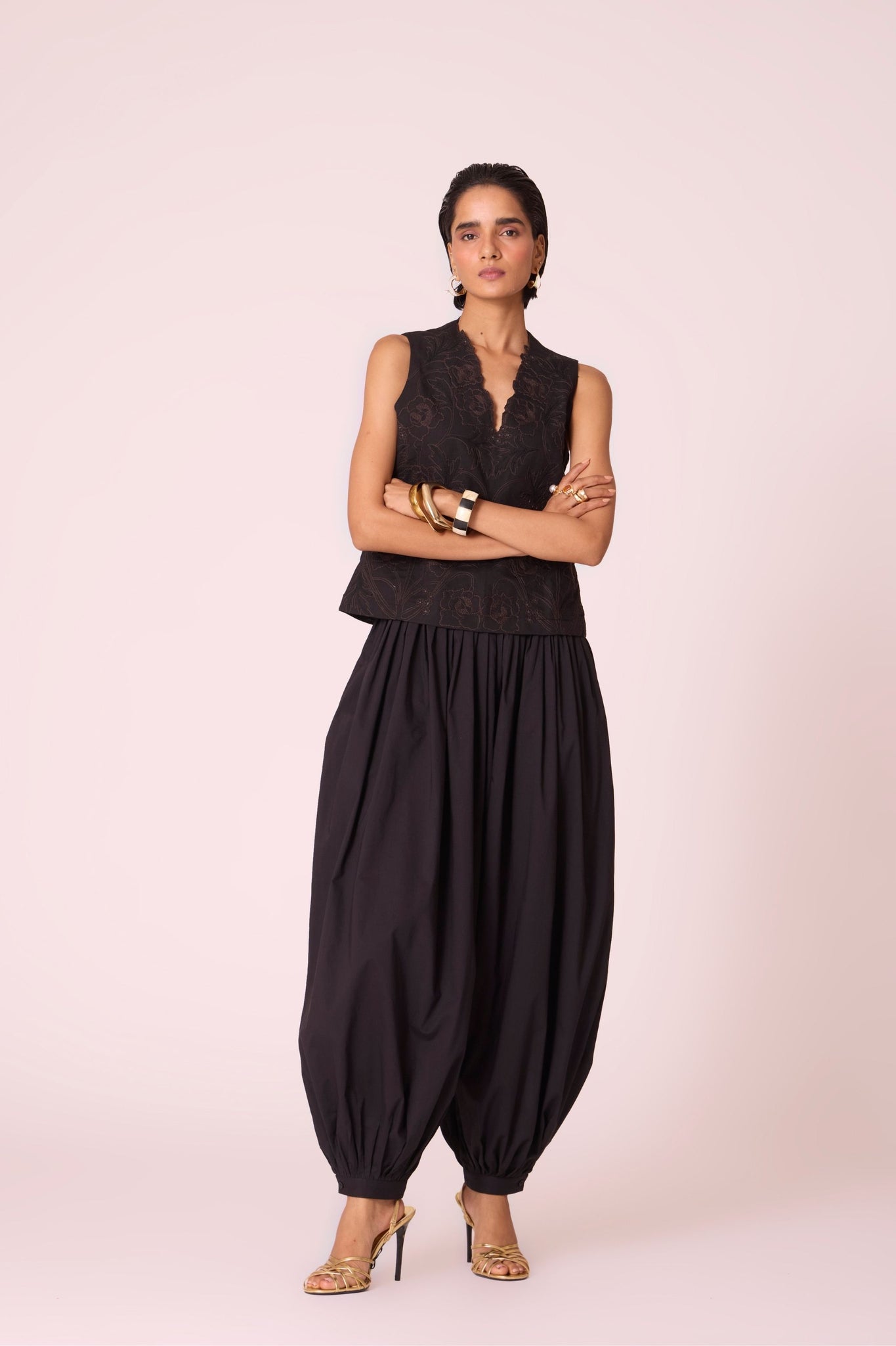 Black organic cotton pleated pants with a relaxed fit, side zip fastening, and adjustable hem cuffs.
