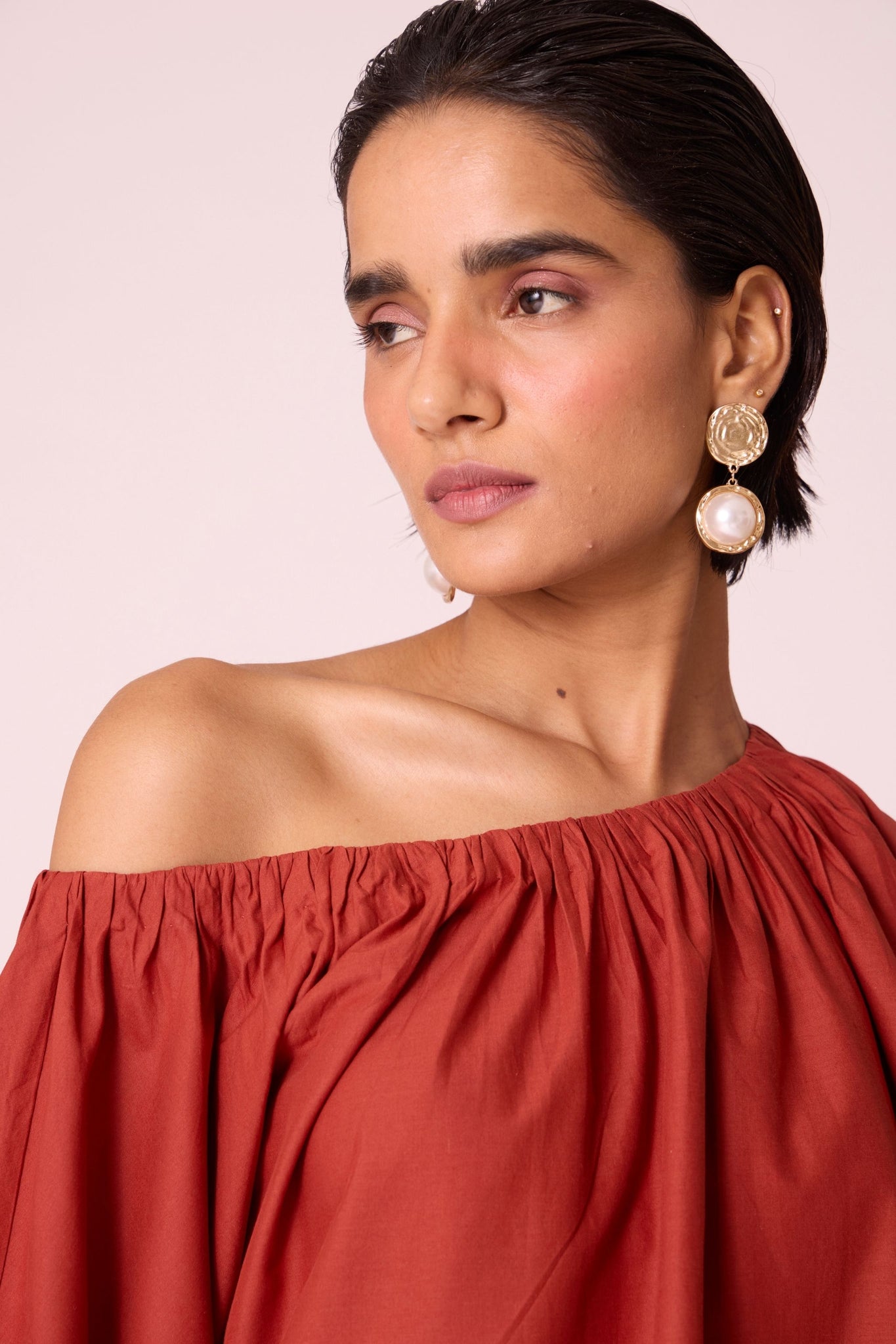 Rust organic cotton off-shoulder top with gathered neckline and pleated sleeve cuffs.