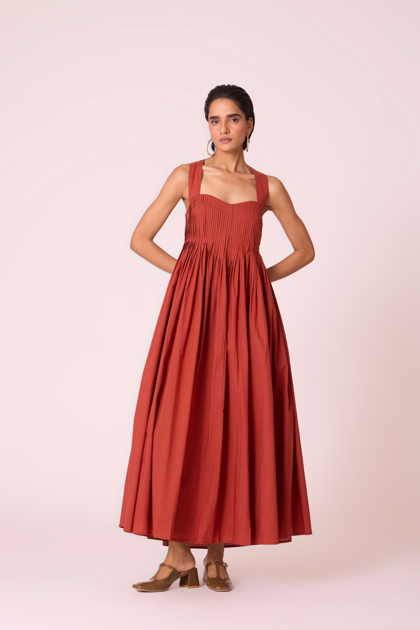 Rust pleated dress in organic cotton voile with a square neckline, thick straps, and a fully lined flared silhouette.

