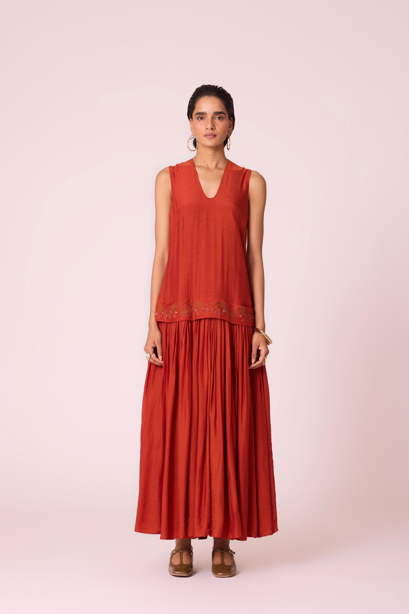 Rust cupro drop-waist dress with hand-embroidered waist, narrow scooped neckline, and full lining.
