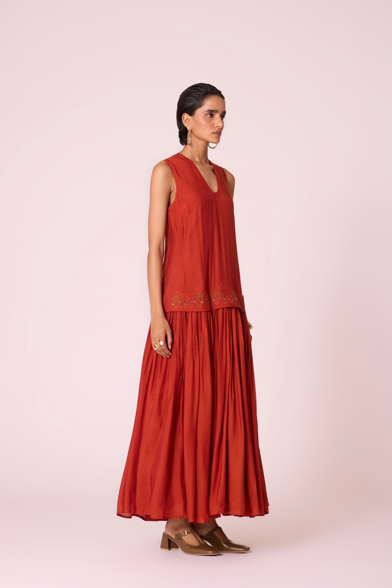 Rust cupro drop-waist dress with hand-embroidered waist, narrow scooped neckline, and full lining.
