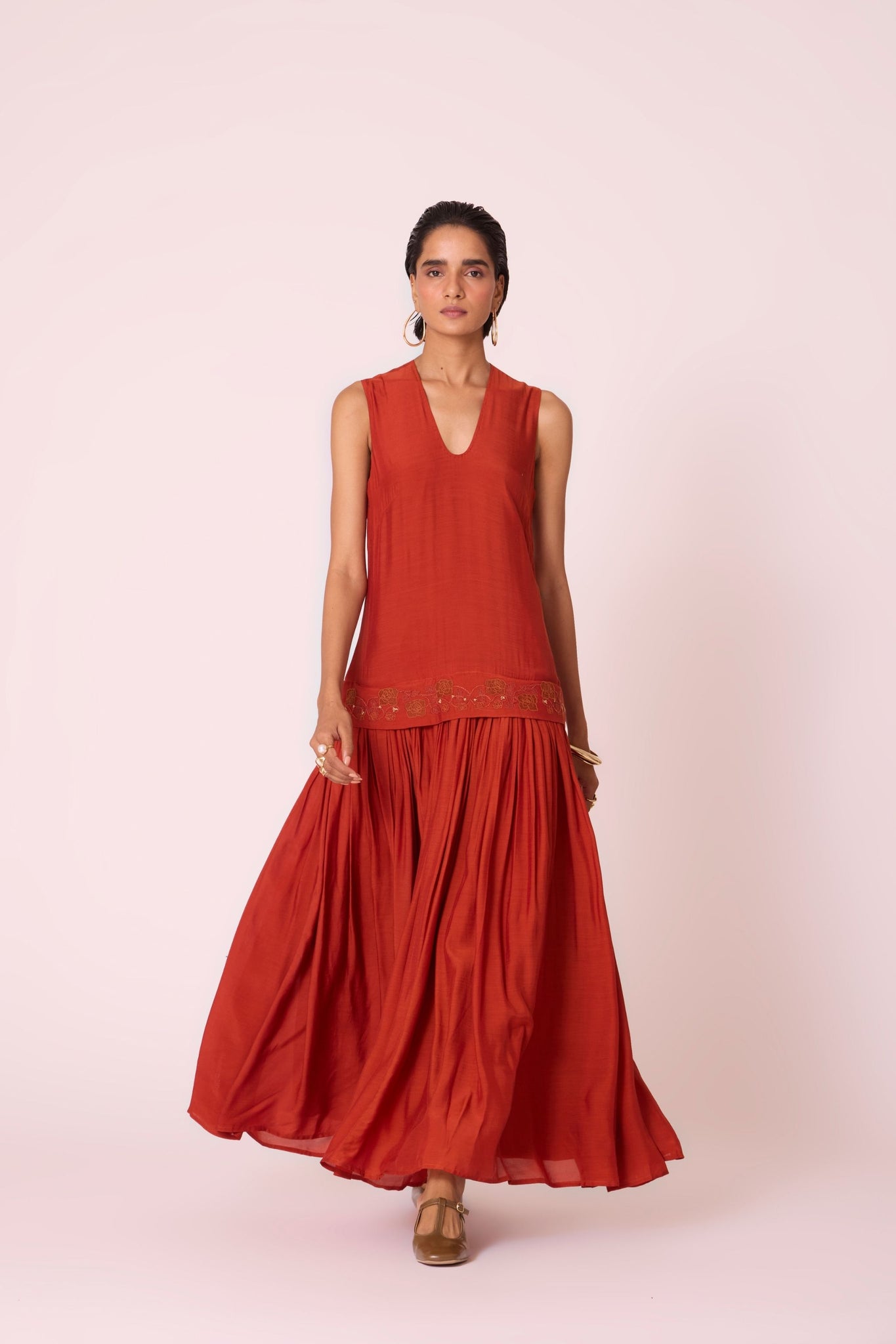 Rust cupro drop-waist dress with hand-embroidered waist, narrow scooped neckline, and full lining.
